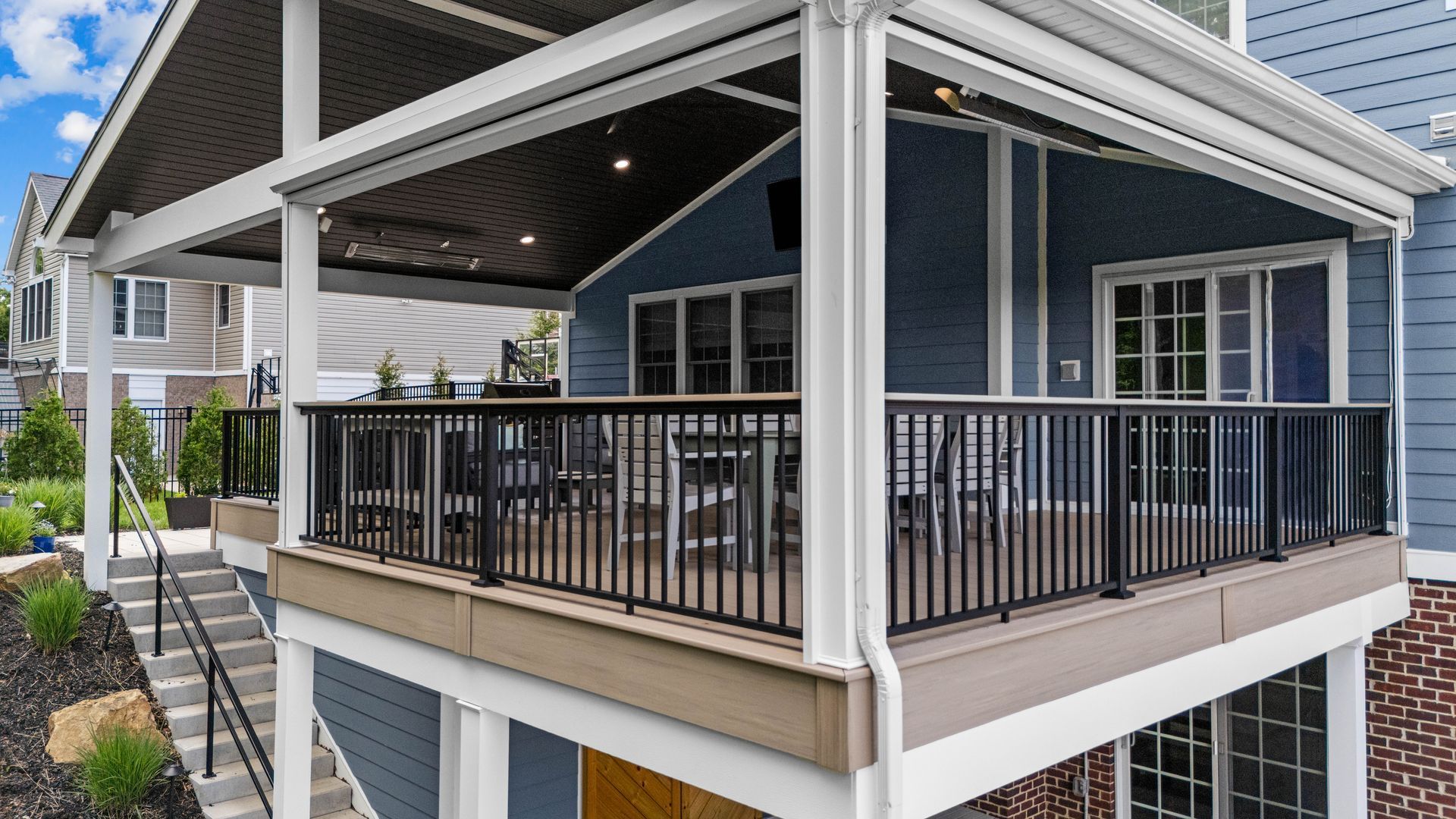 Covered porch with black railing on a blue house, viewed from the corner.