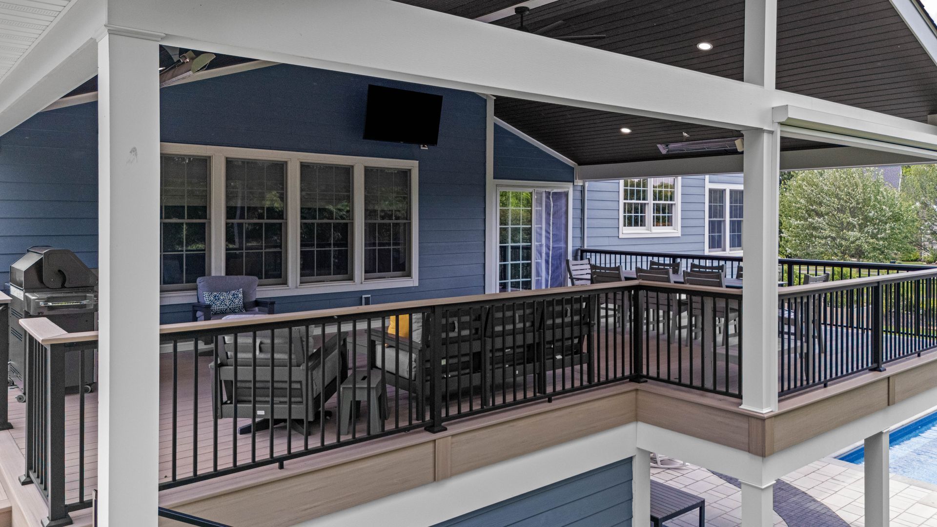 Covered outdoor patio with black railing, tables, and chairs overlooking a pool area