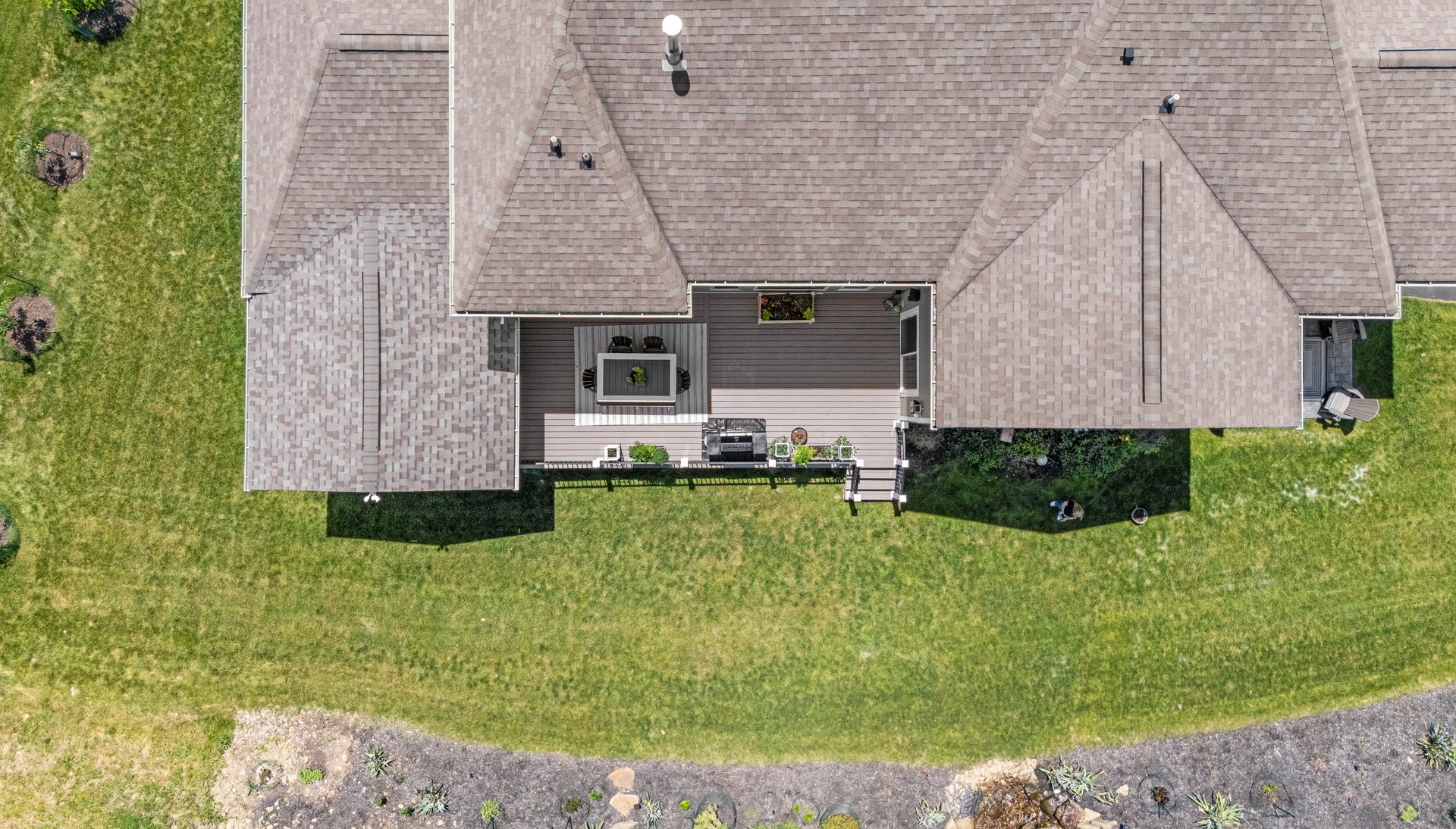 Aerial view of a suburban house with a gray roof, patio, and green lawn beside a road.