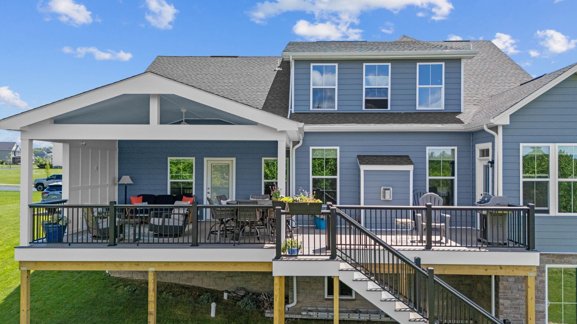 Gray house with elevated front porch, white trim, black railings, and stairs leading up from the yard