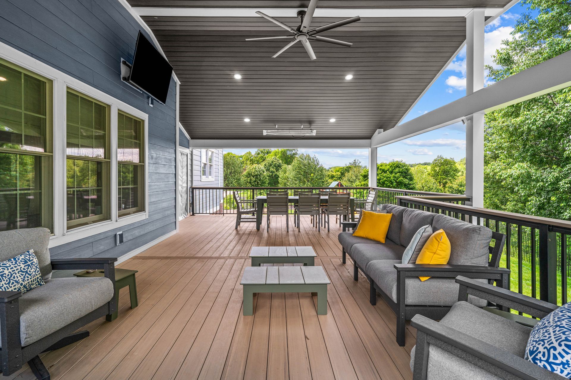 Covered porch with wicker seating, yellow cushions, and dining table overlooking a green yard