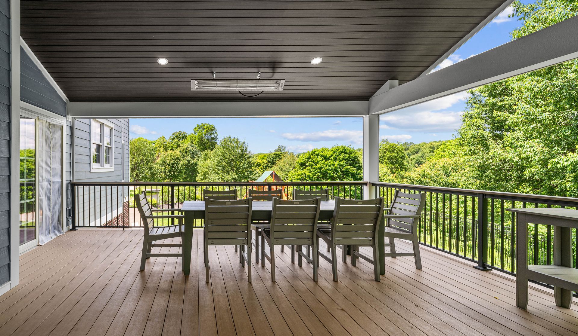Covered wooden deck with dining table and chairs overlooking green trees and a lake.