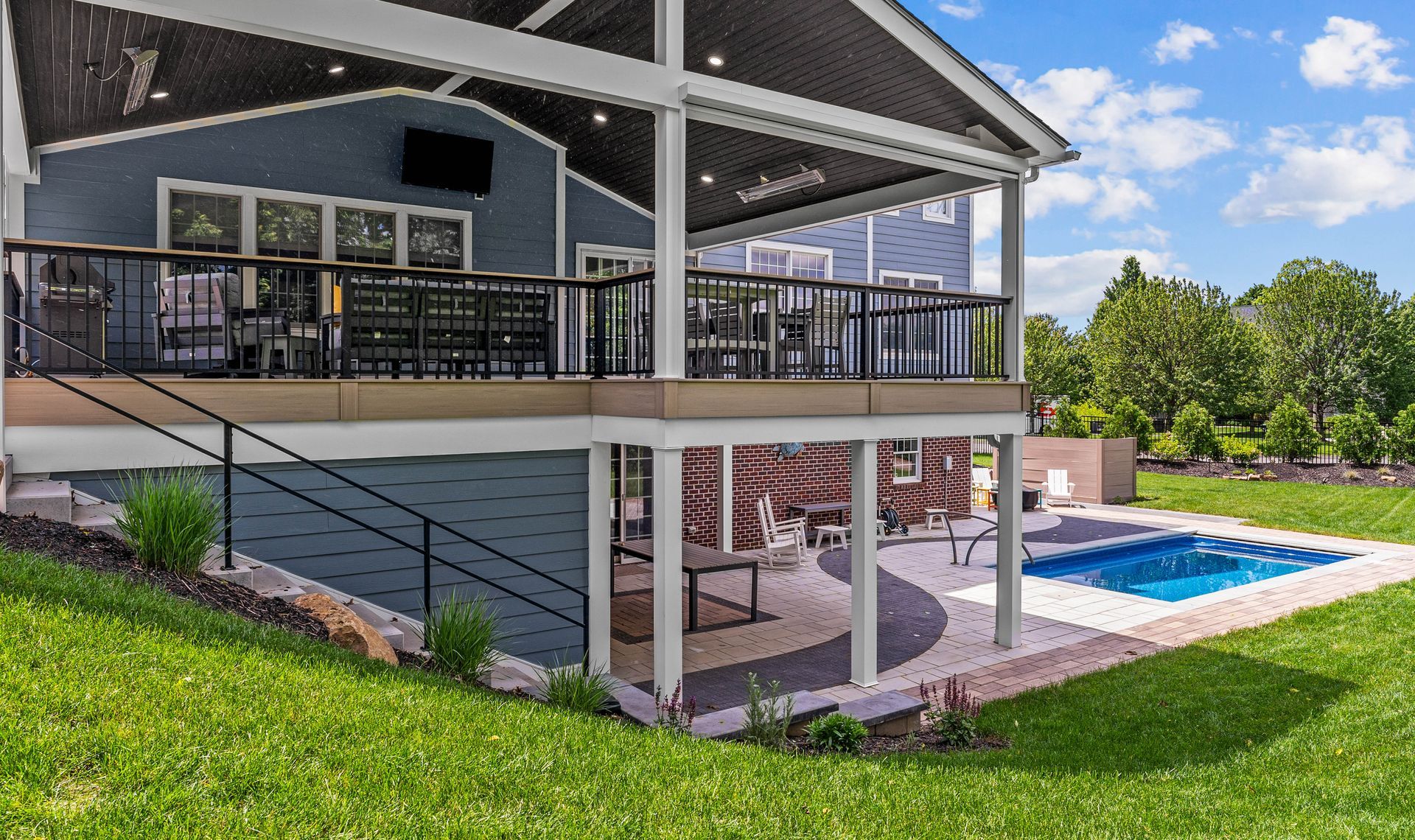 Two-story house with a covered deck and pool in the backyard, viewed from a grassy slope.