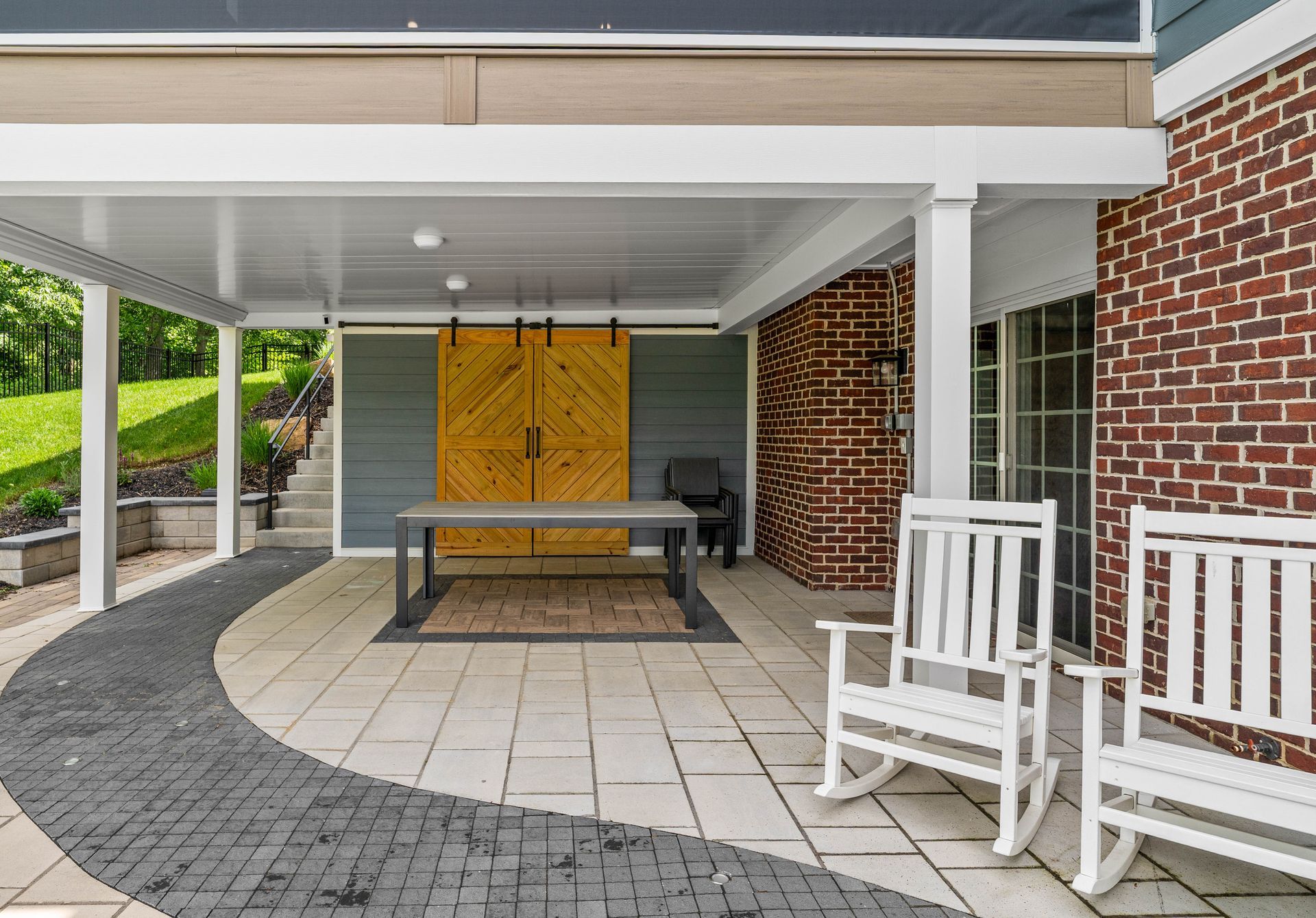 Covered brick patio with white rocking chairs, table, and yellow double doors leading indoors