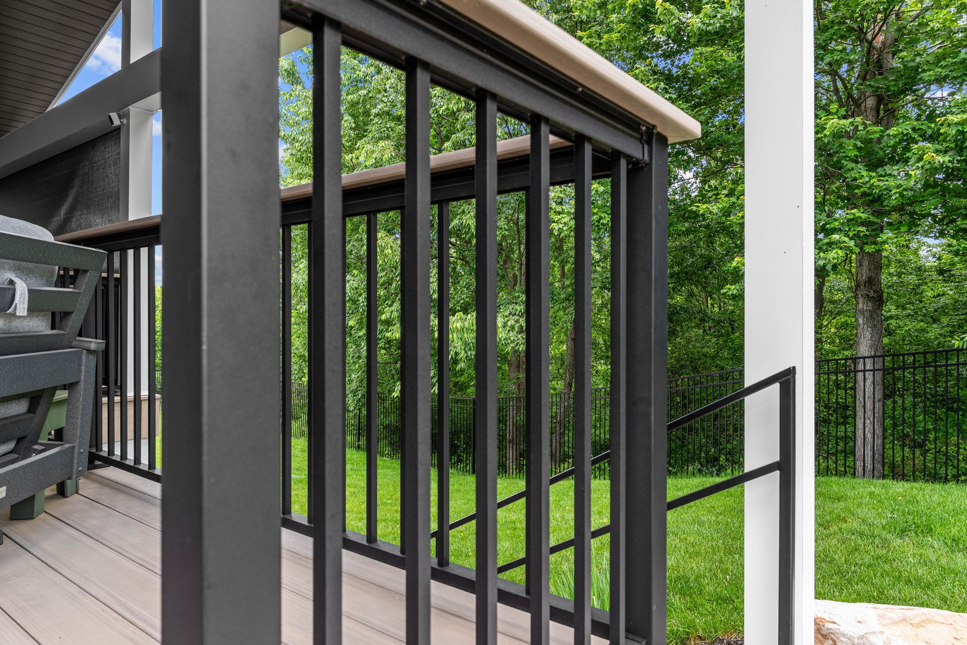 Black porch railing beside a deck with green lawn and trees beyond