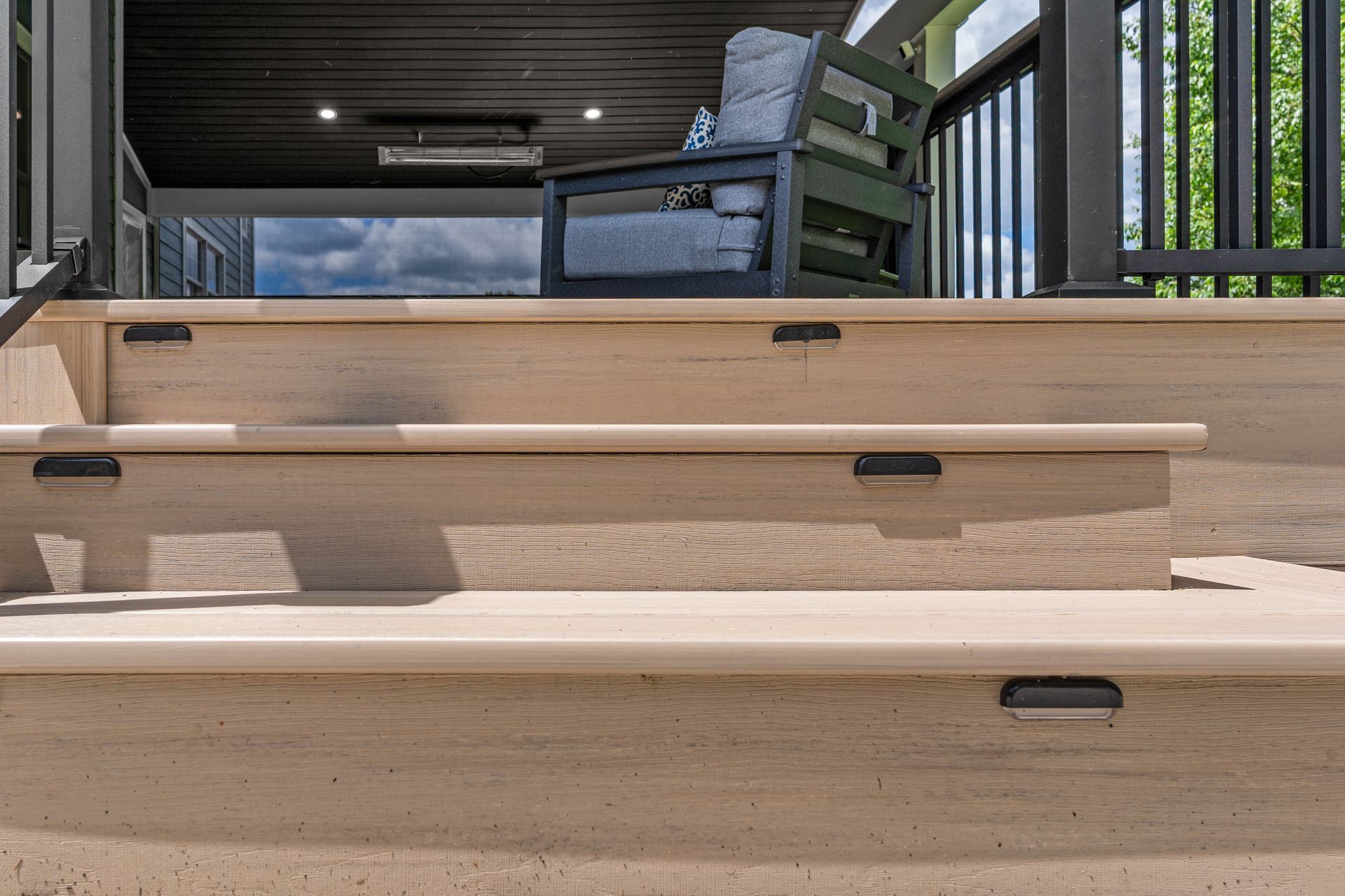 Wooden deck stairs leading to a covered patio with a blue chair and railing.