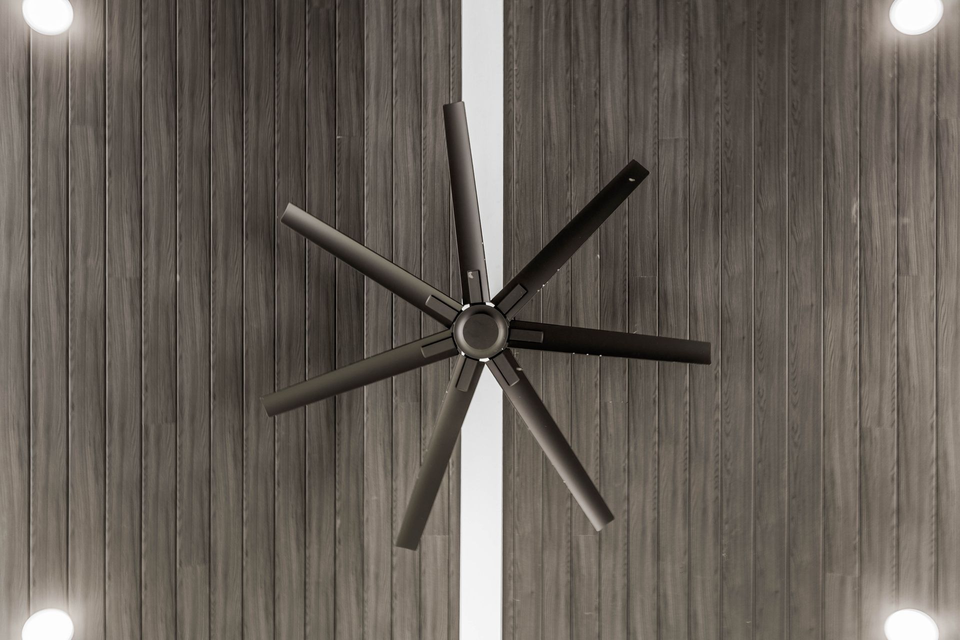 Large black ceiling fan on a wood-paneled ceiling with recessed lights