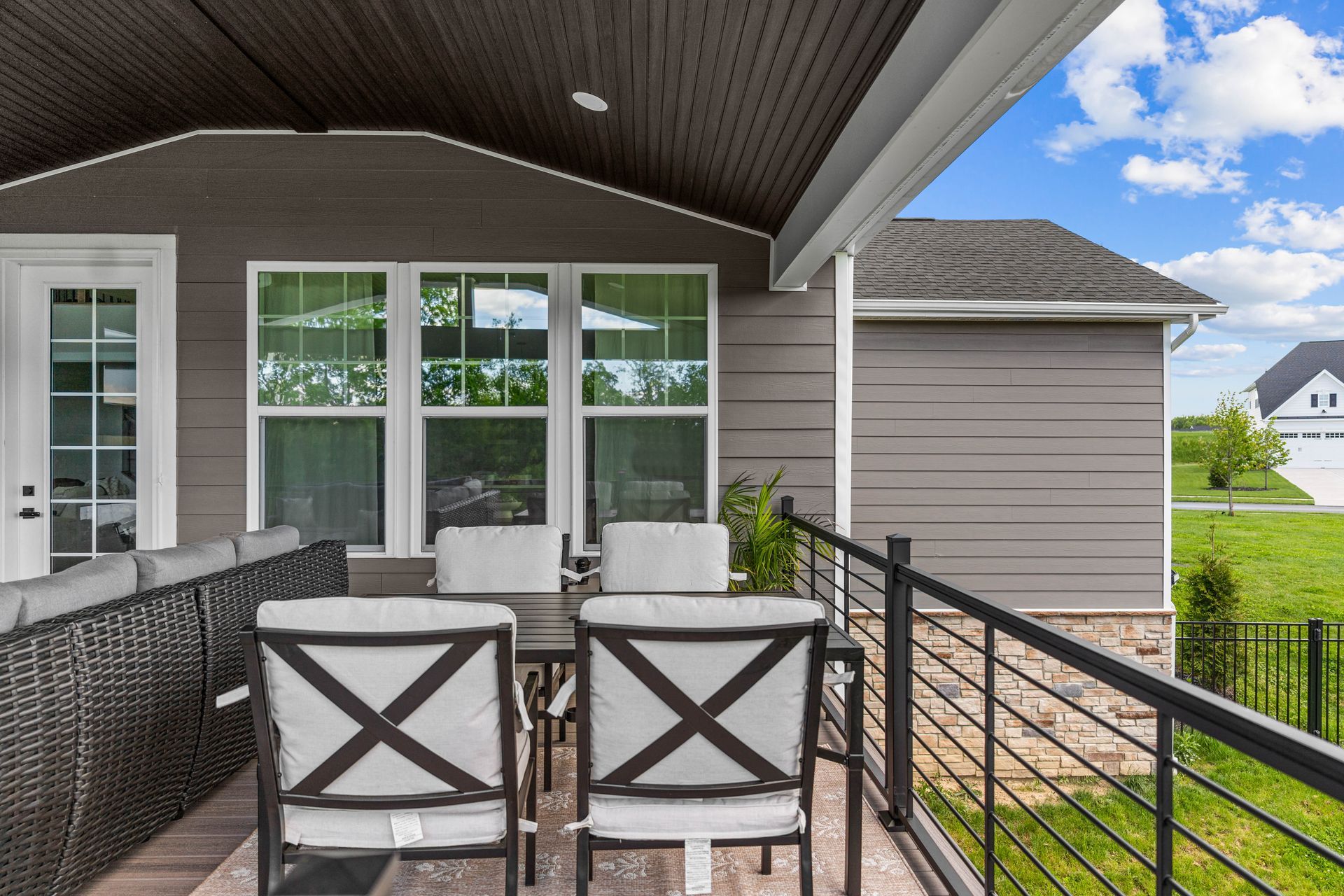 Covered balcony with wicker chairs, railing, and a view of the yard and neighboring house.