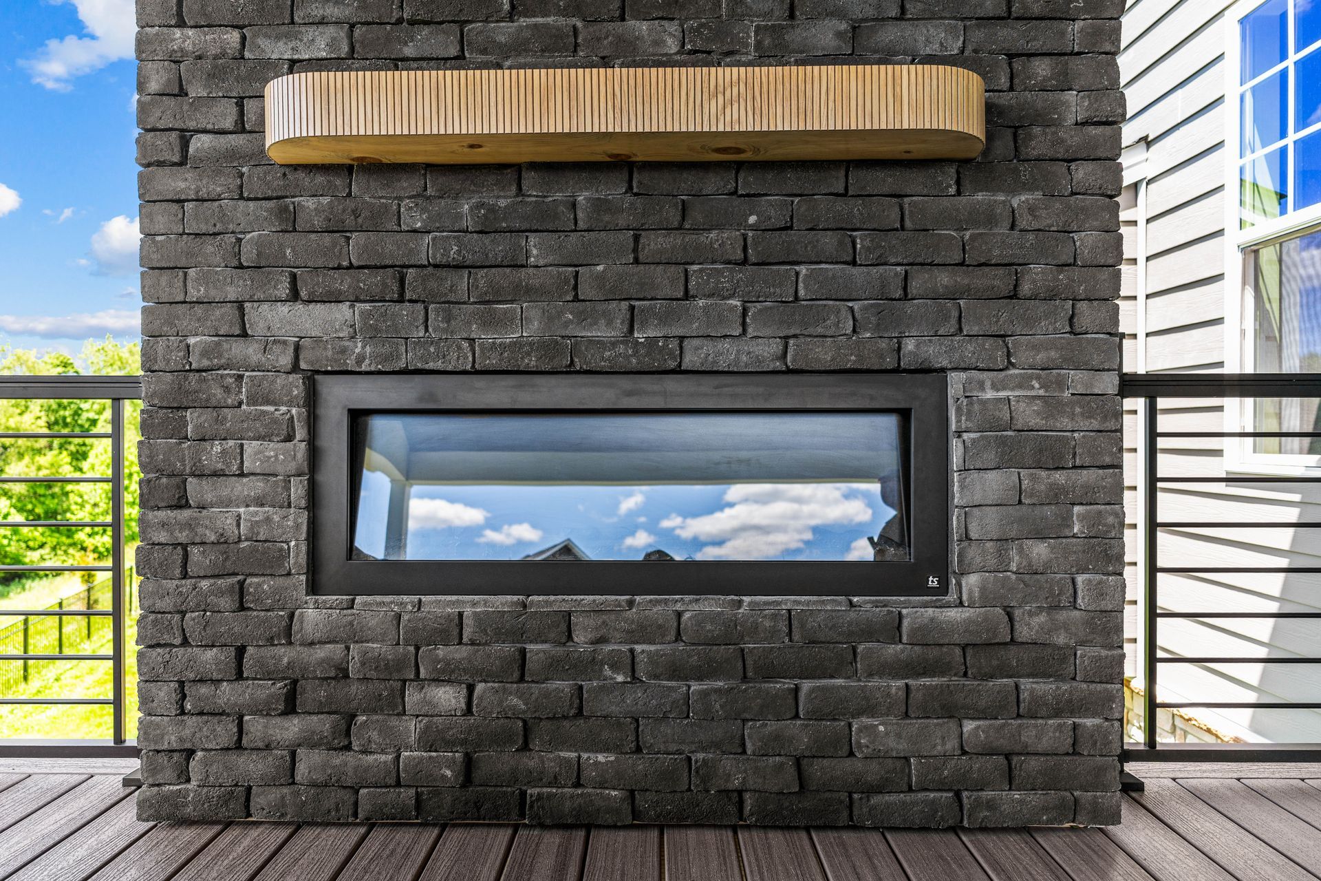 Brick outdoor fireplace with a long horizontal firebox and wooden mantel on a deck