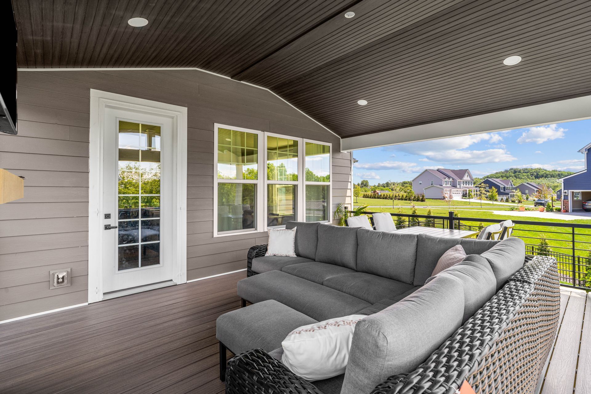Covered patio with gray sectional seating, French doors, and a view of a grassy neighborhood pond