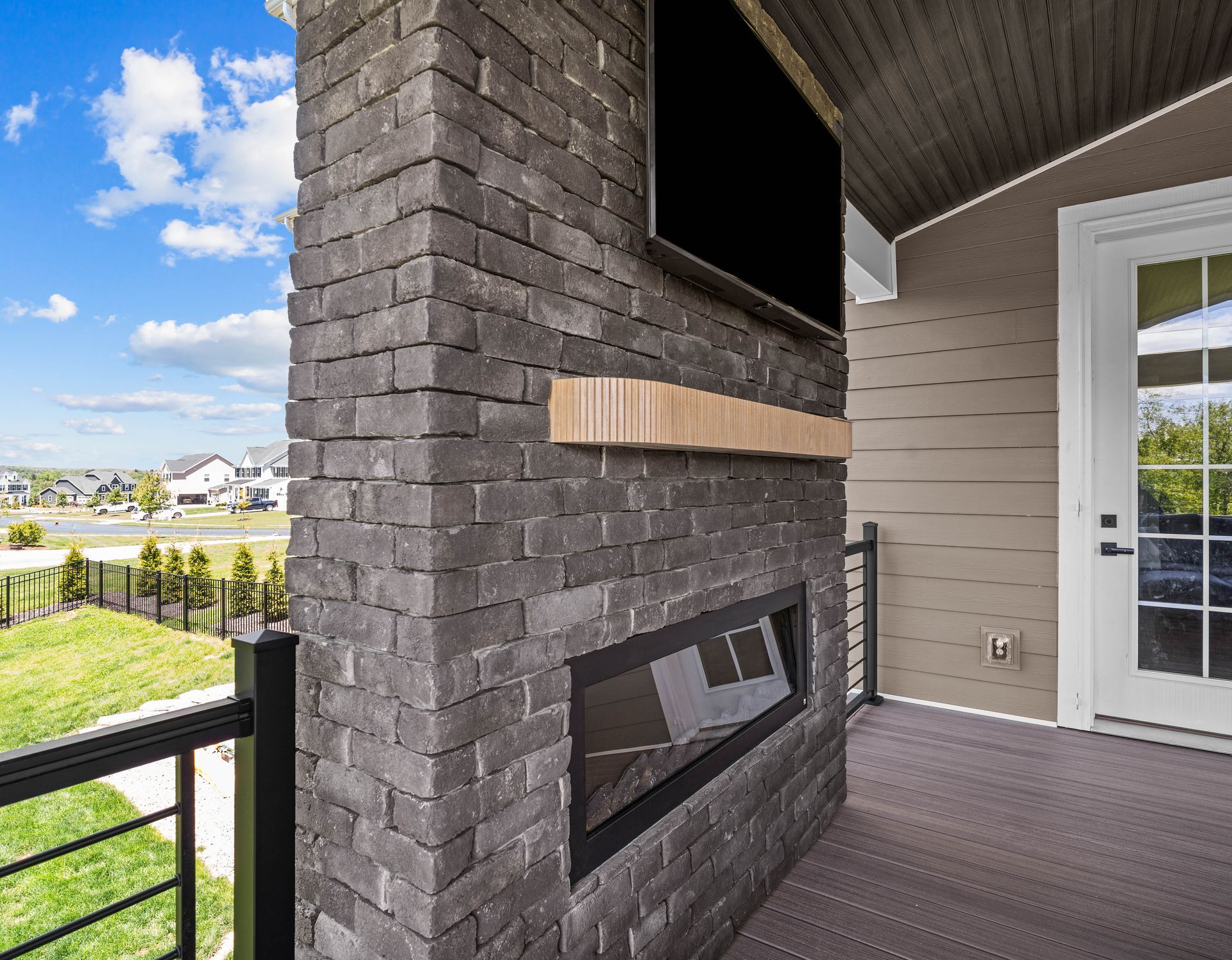 Covered patio with a stone fireplace, TV niche, and sliding glass door overlooking a green neighborhood.