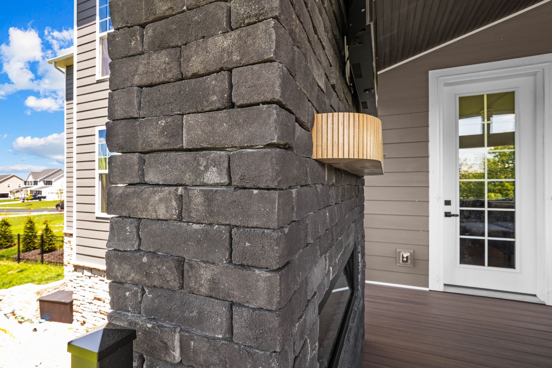 Front porch with dark stone column, wood wall, and white glass-paneled door