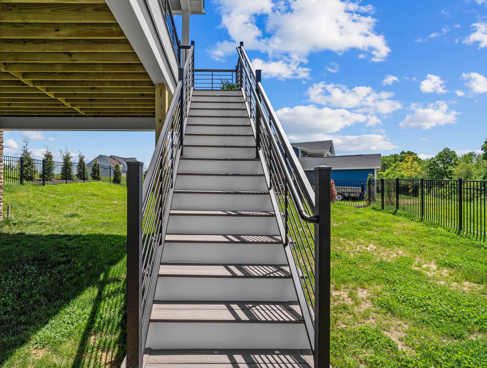 Outdoor metal staircase leading to a raised deck in a grassy yard under a blue sky