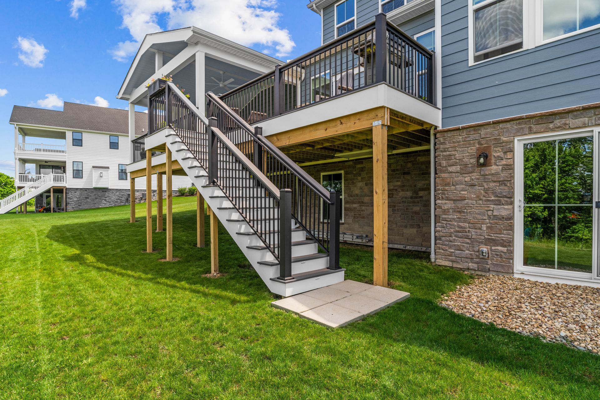 Backyard stairs to an elevated deck on a blue house with brick foundation and green lawn