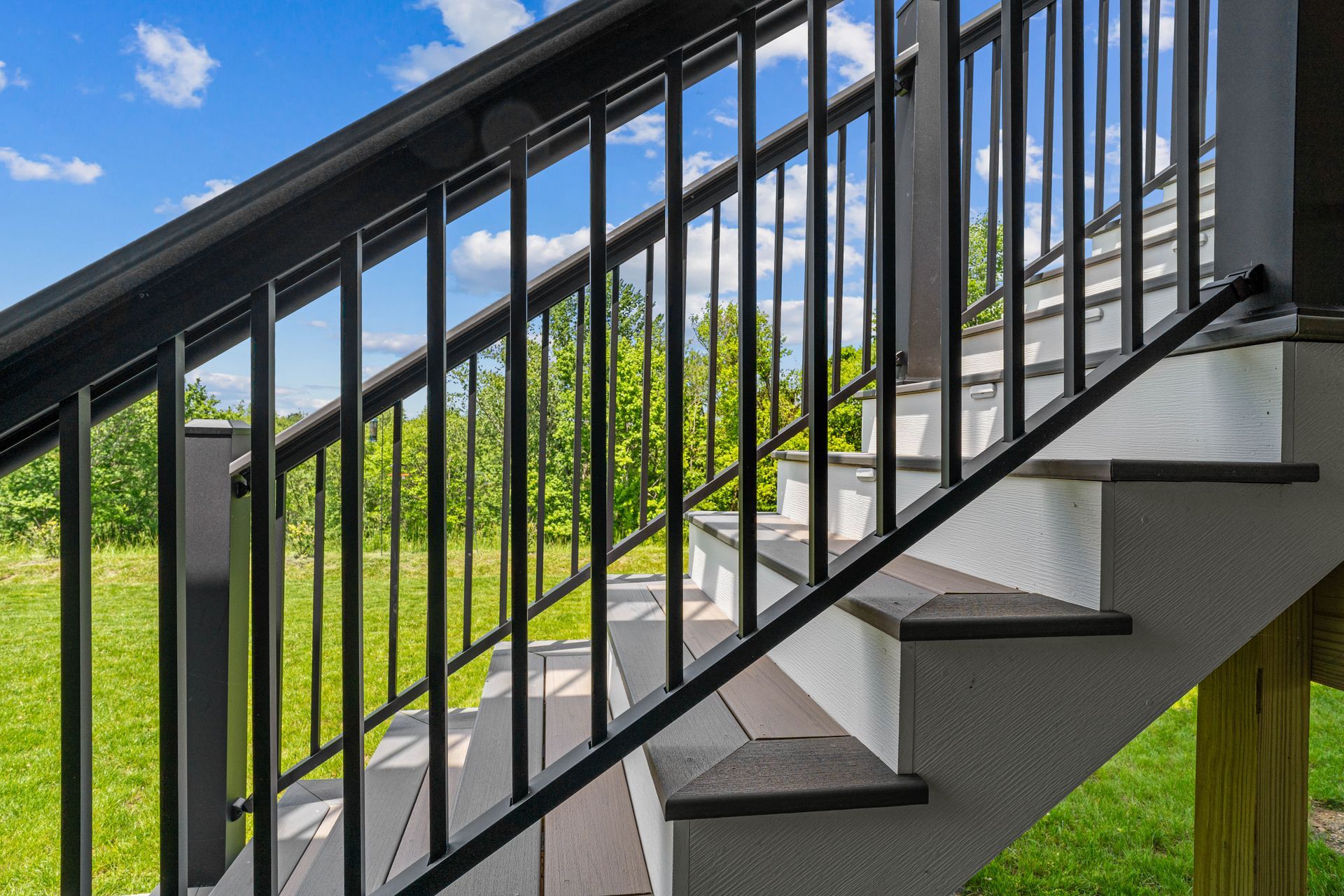 Black metal staircase with white steps beside a green lawn and blue sky