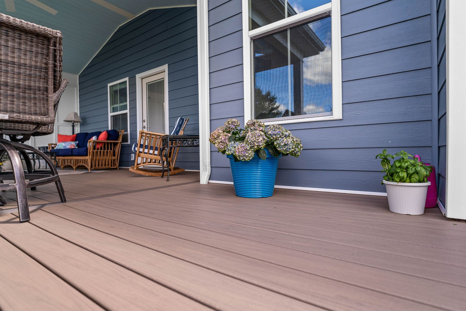 Blue house porch with tan deck, wicker chair, and flower pots by the wall