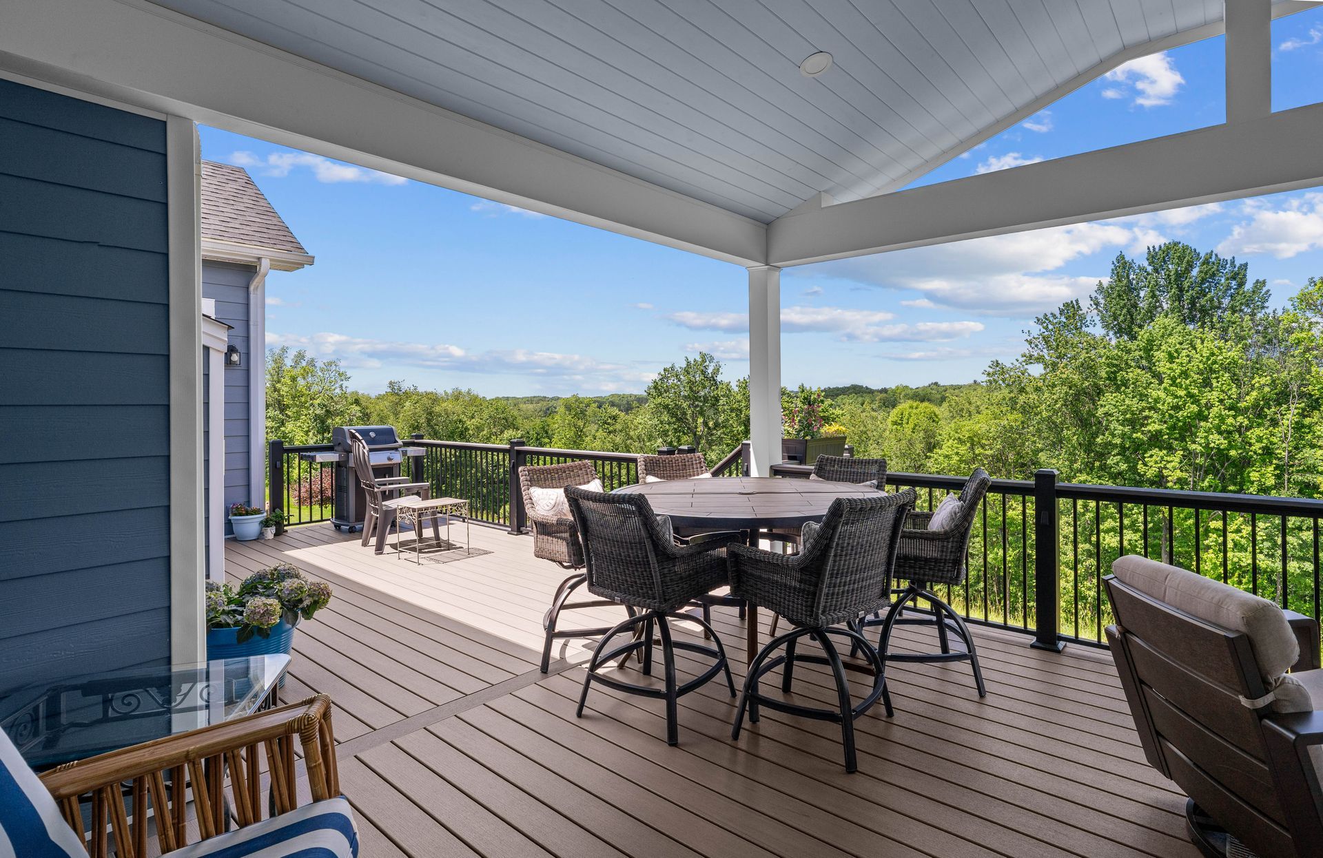 Covered patio with dining table, chairs, and a view of green trees and blue sky