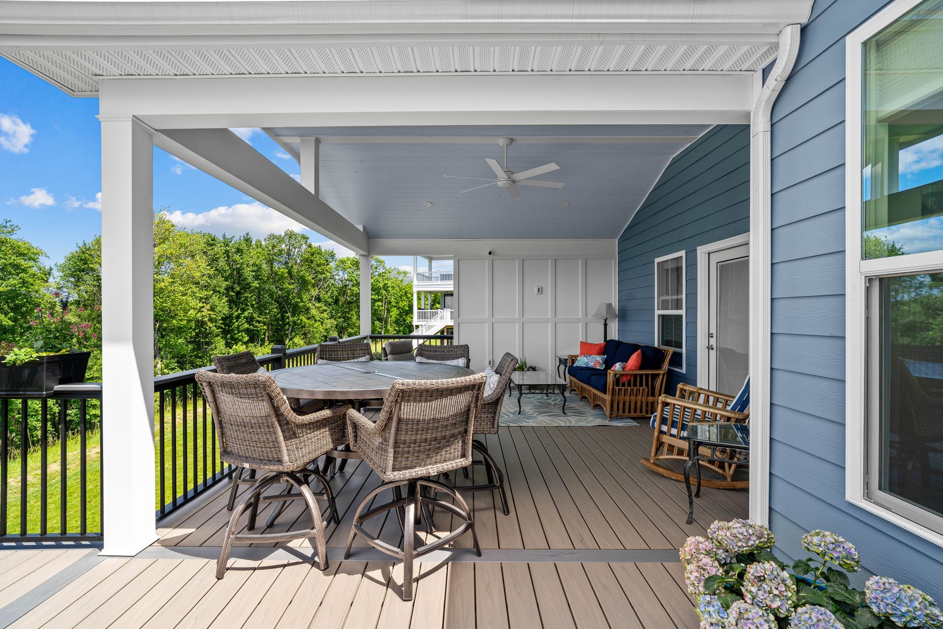 Spacious covered porch with wicker table and chairs, blue siding, white trim, and open backyard view