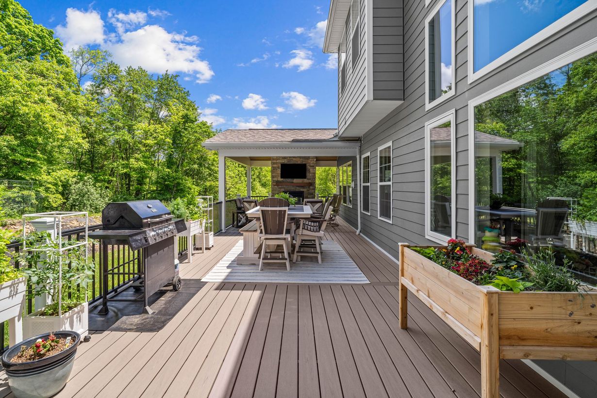 Modern deck with grill, dining table, raised planter, and house exterior on a sunny day