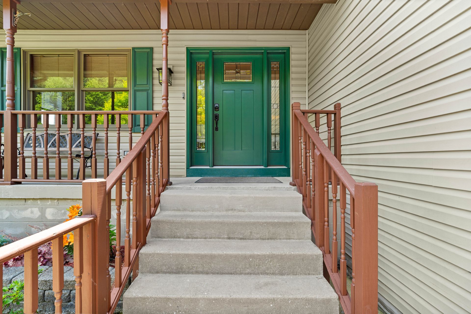 Front porch with green double doors, concrete steps, and wooden railings under a covered entryway