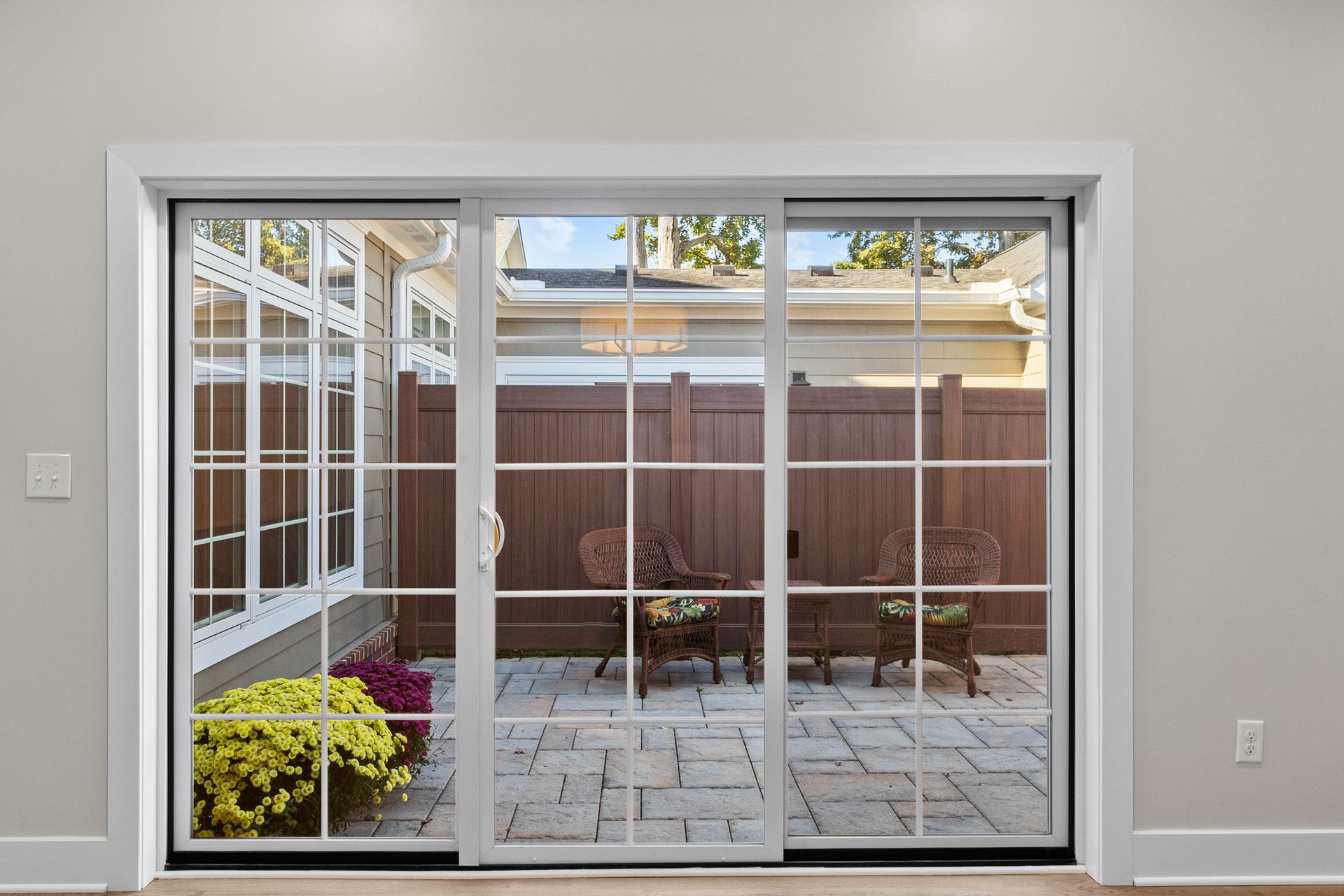 Sliding glass doors open to a small brick patio with a wooden fence and potted flowers.