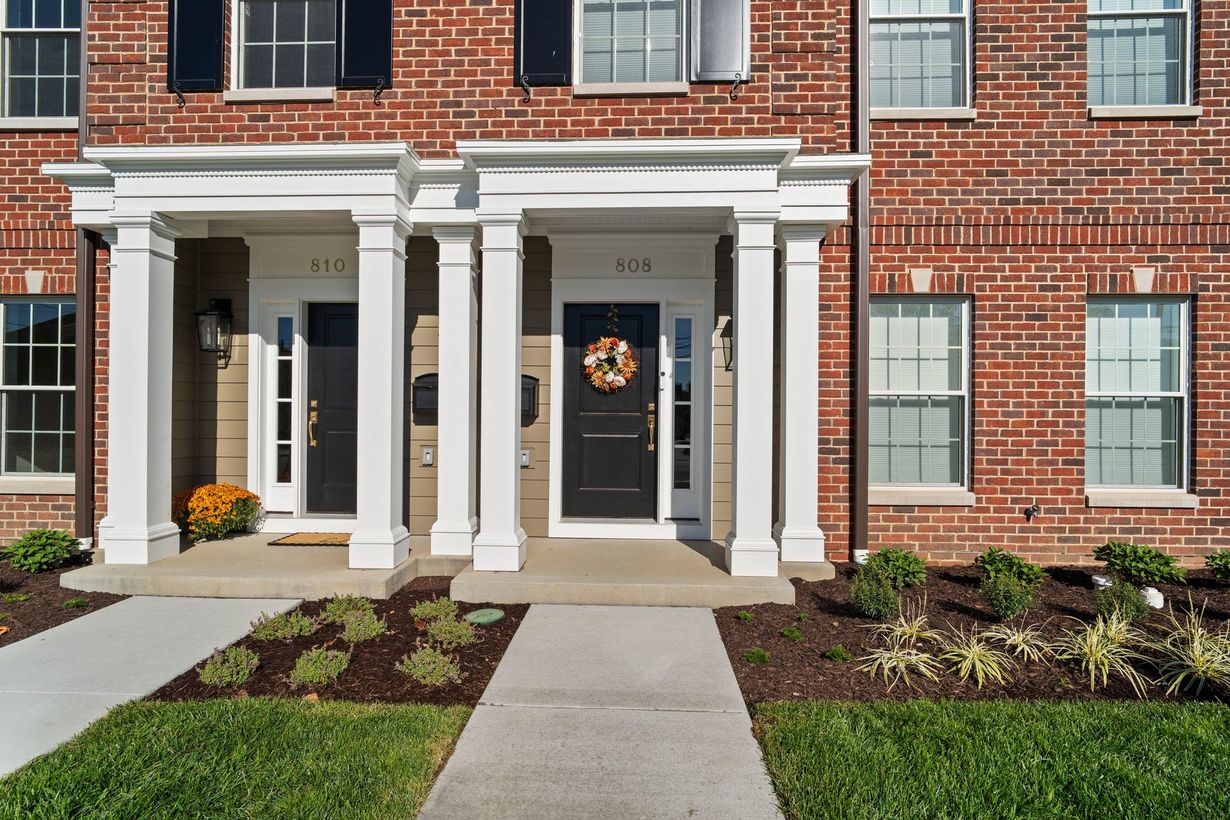 Brick apartment entrance with white columns, dark doors, and landscaped walkway