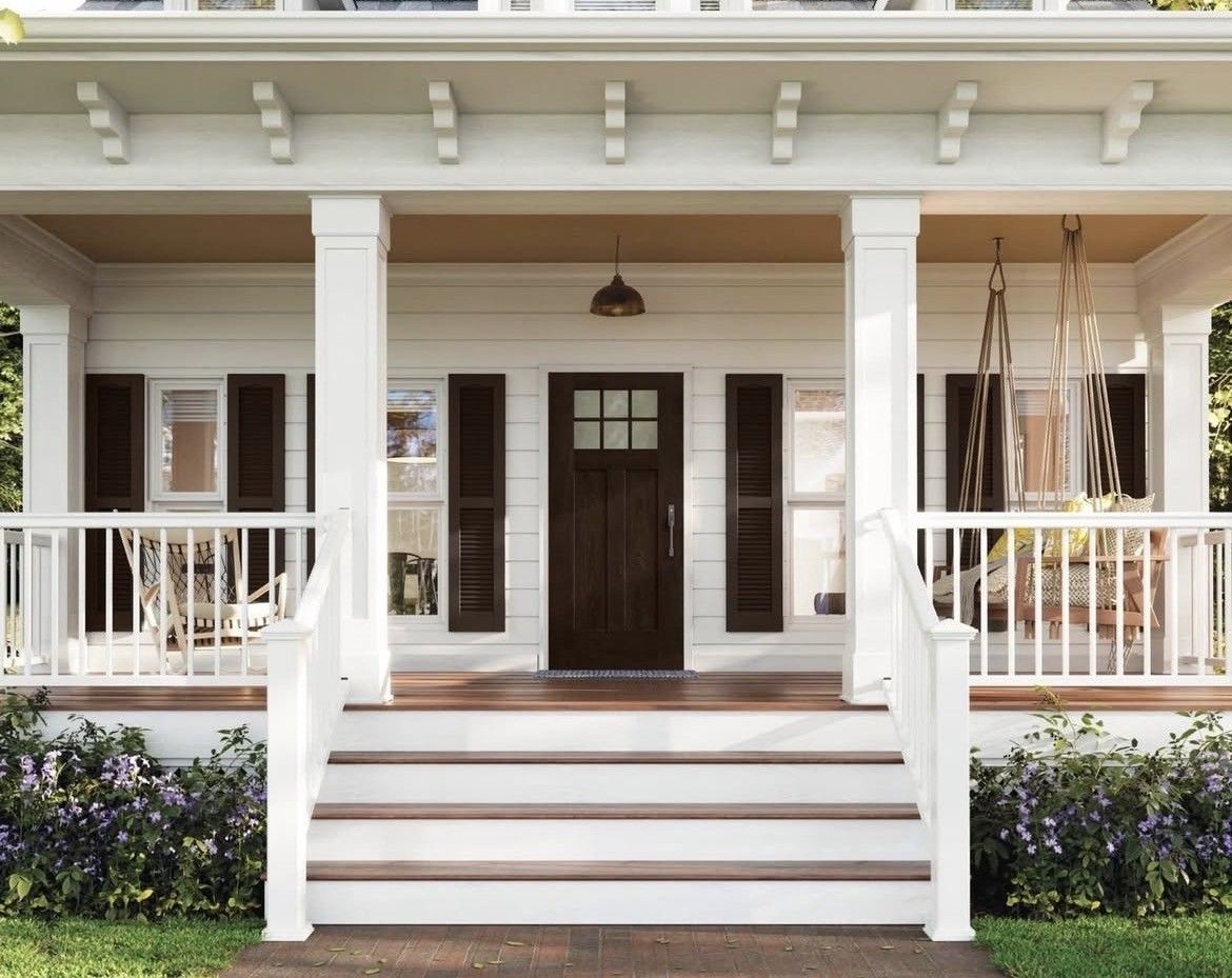 White porch with steps, columns, and a dark brown front door, surrounded by greenery.