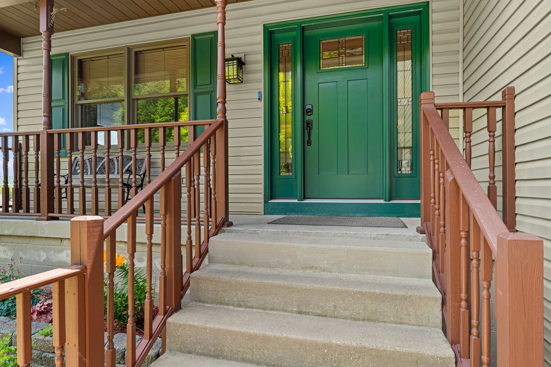 Front porch with green door, steps, and brown railings on a beige house.