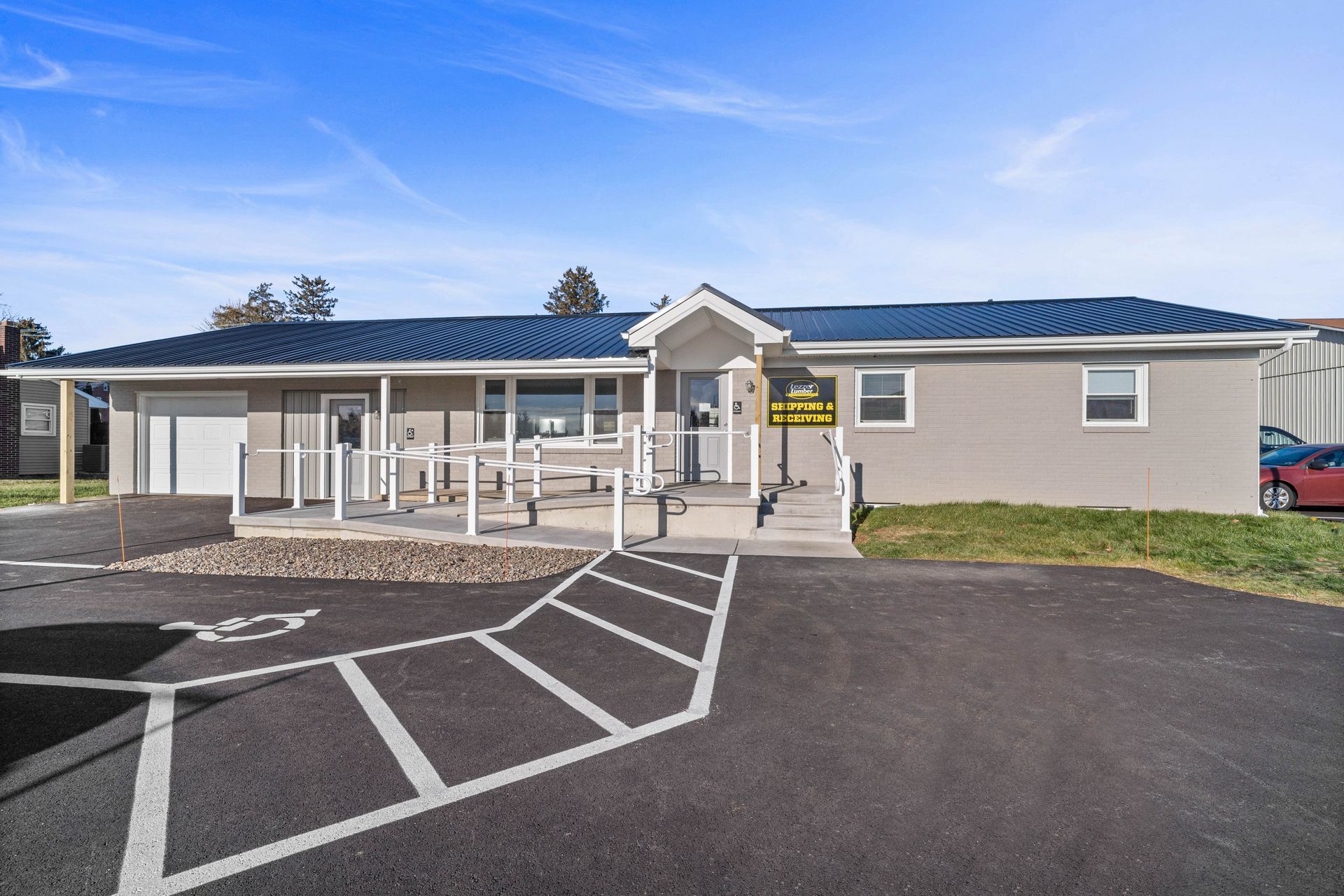Single-story beige building with blue roof and covered entrance, beside an empty parking lot.