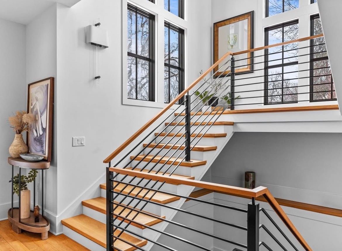 Wooden staircase with metal railing and light-colored walls and windows.