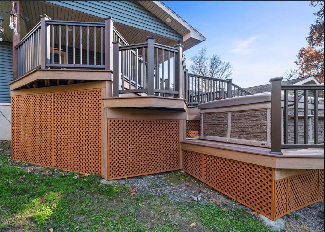 Wooden deck with brown lattice skirting, railings, and steps. Green grass and blue sky background.
