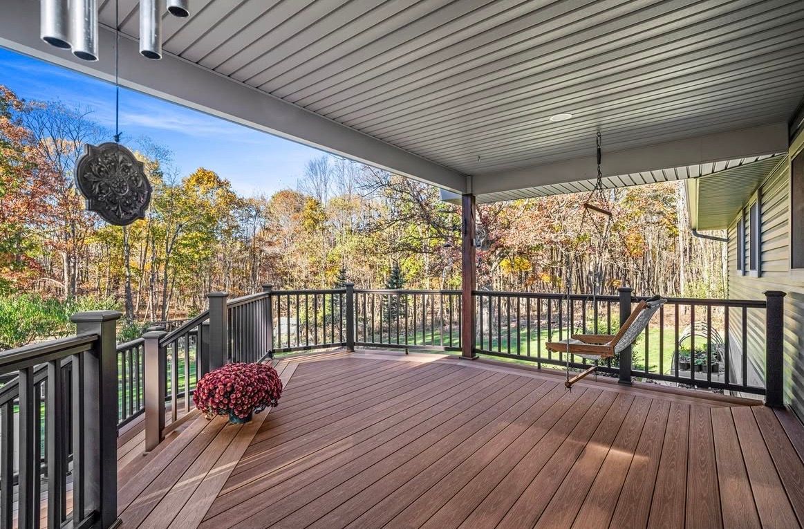 Covered wooden deck overlooking autumn trees; swing, wind chimes, and railing present.