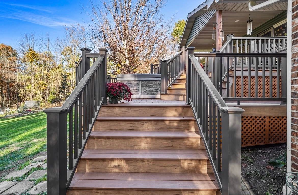 Wooden stairs leading up to a deck with a hot tub and railings, surrounded by grass and trees.