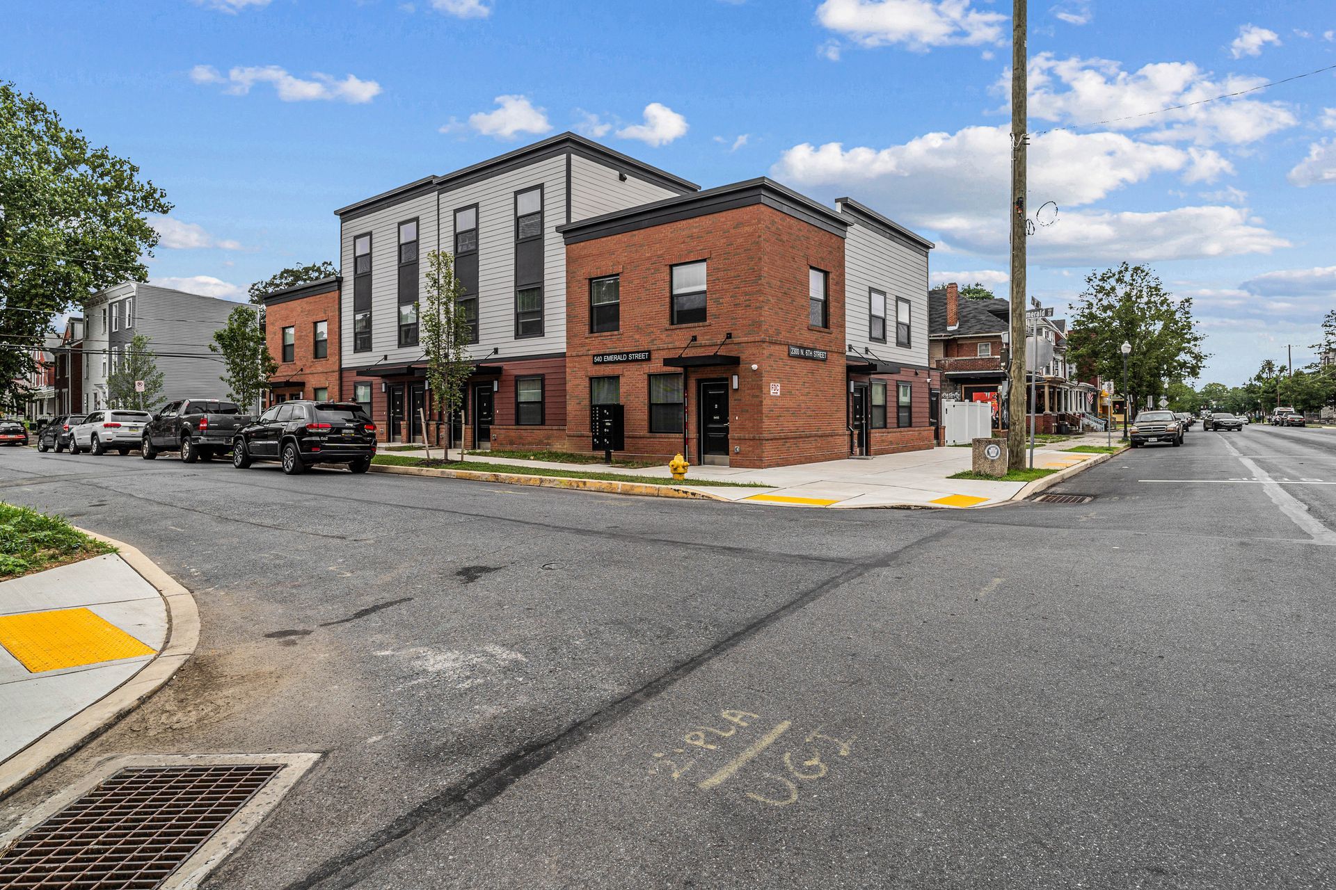Street corner with modern brick building, parked cars, and a wide intersection on a sunny day