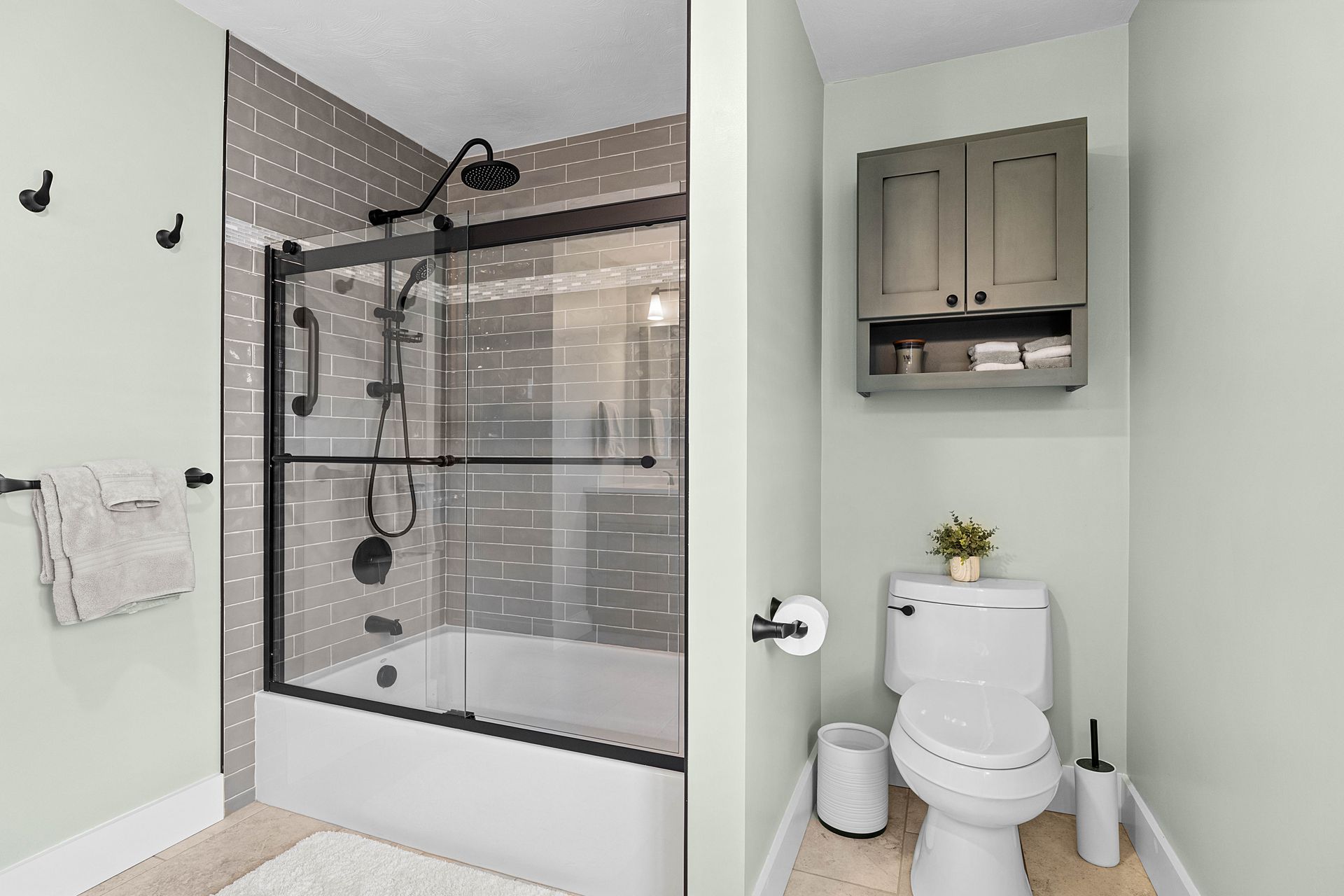 Modern bathroom with glass shower, white toilet, and wall cabinet on pale green walls.