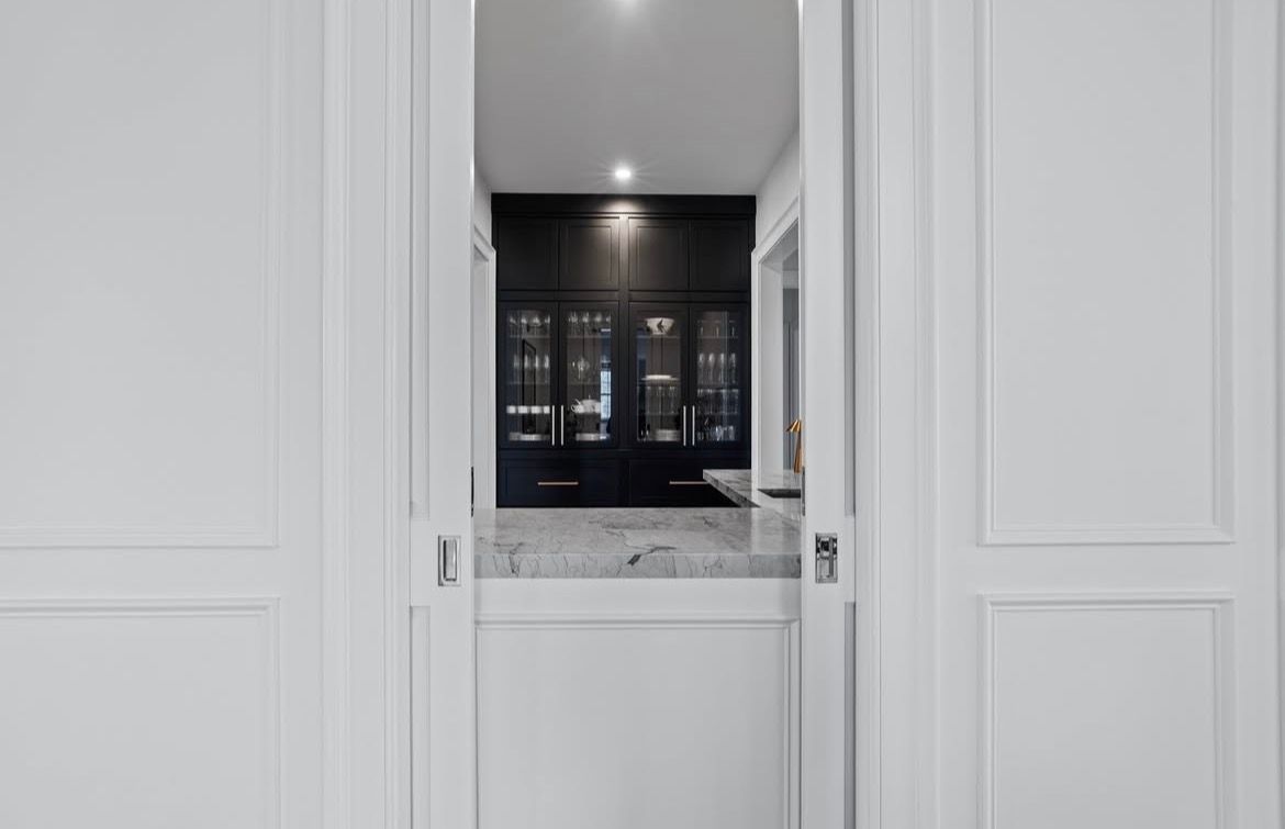 White pocket doors open to reveal a dark-cabinet bar area with a marble countertop.