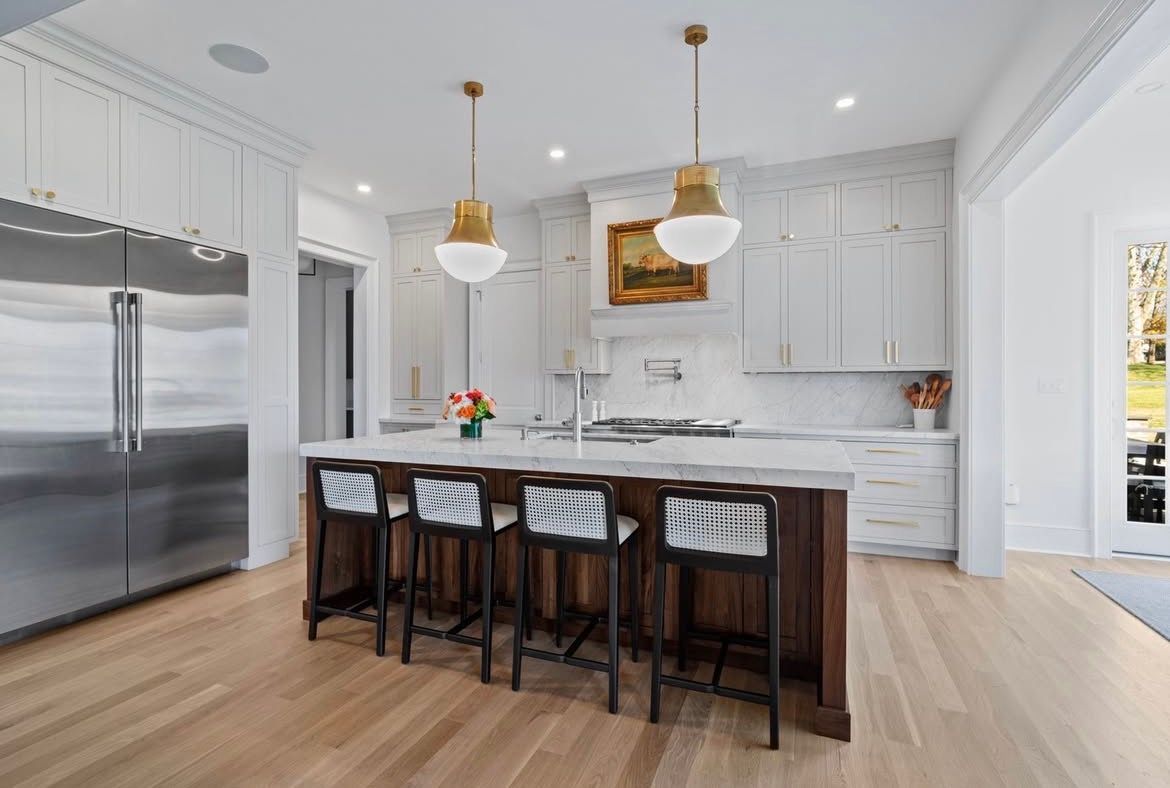 Modern kitchen with island, marble countertops, pendant lights, stainless steel fridge, wood floor.