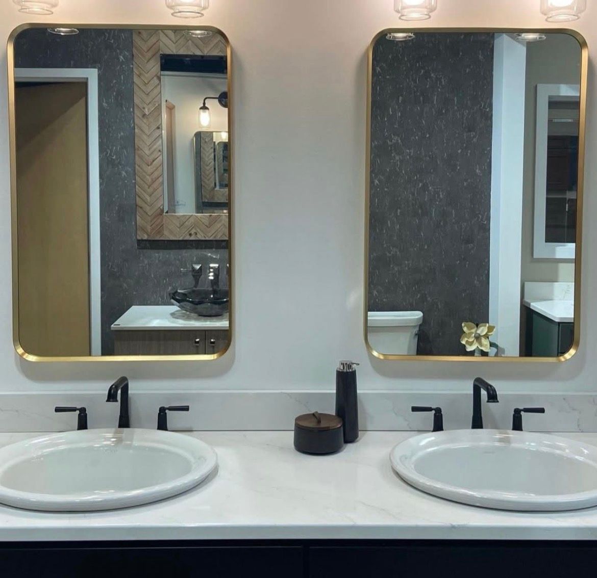 Two gold-framed rectangular mirrors above white sinks with black faucets. Cream countertop and dark cabinets.