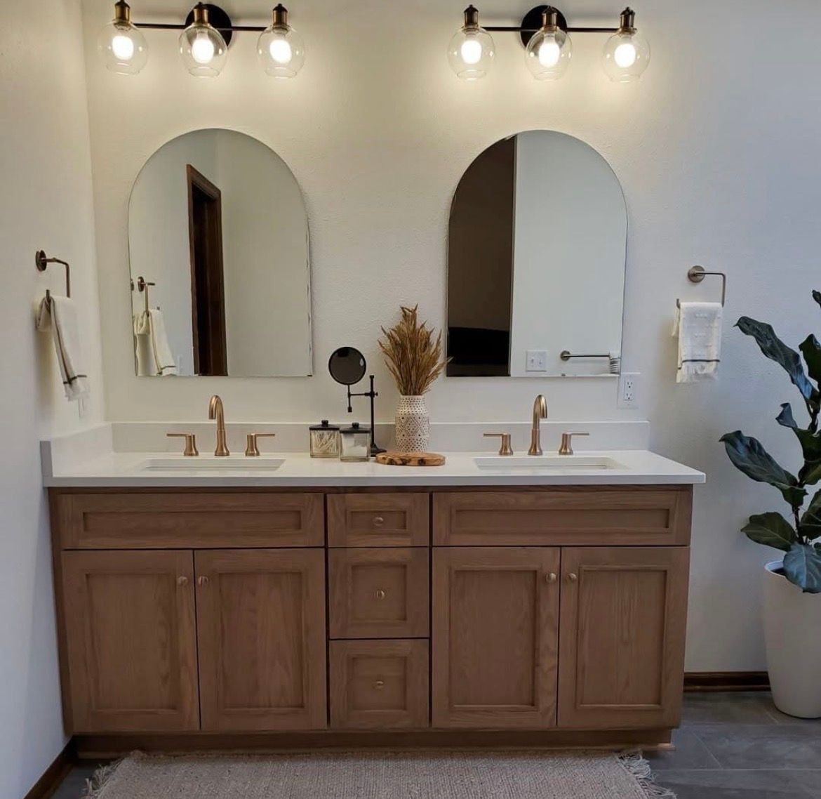 Bathroom with two sinks, two mirrors, gold frames, black faucets, and countertop with accessories.