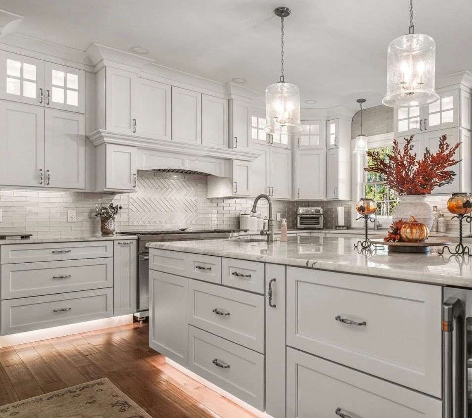 White kitchen with island, cabinets, and pendant lights. Wooden floor with warm lighting.