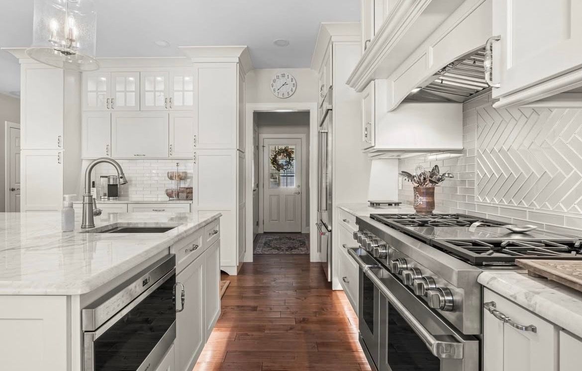 Bright white kitchen with large island, pendant lights, and arched window overlooking trees.