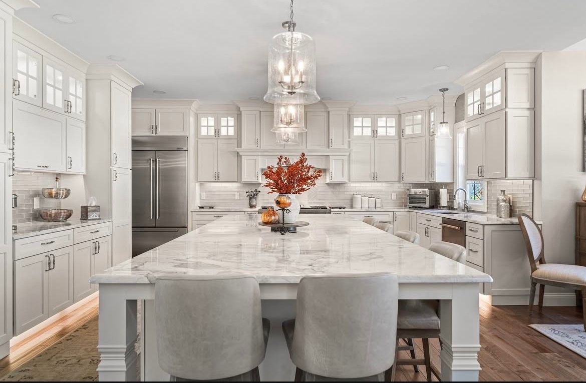 Elegant white kitchen with large island, stainless steel appliances, and two hanging pendant lights.