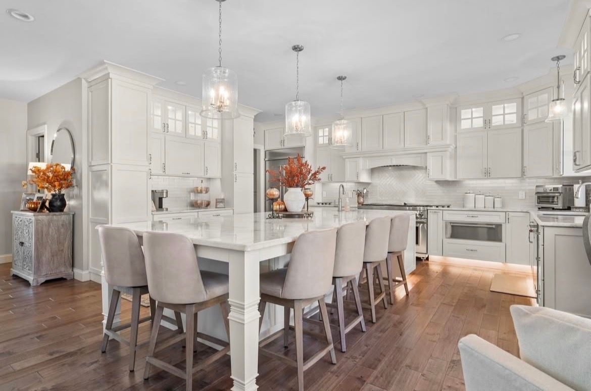 Bright white kitchen with large island, pendant lights, wooden floor, and bar stools.