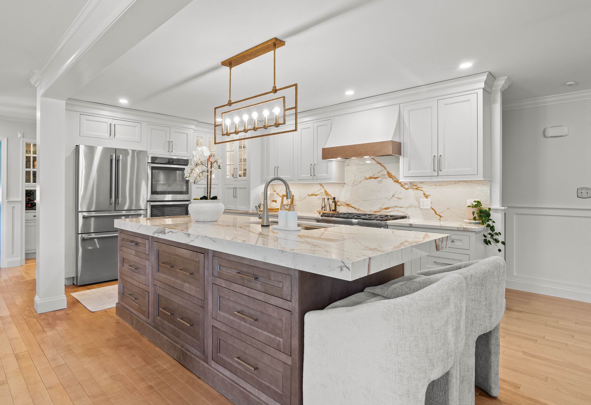 Bright modern kitchen with large island, marble counters, white cabinets, and stainless steel appliances.