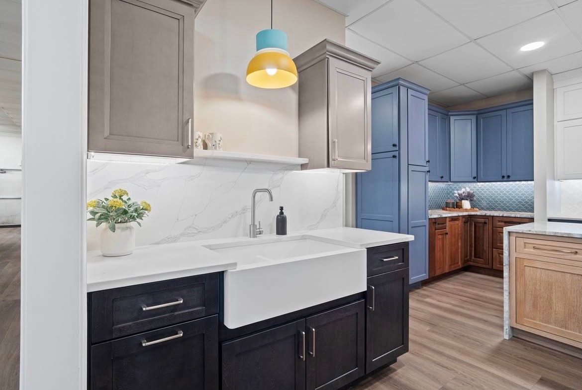 Kitchen display with various cabinet colors, a white farmhouse sink, and under-cabinet lighting.