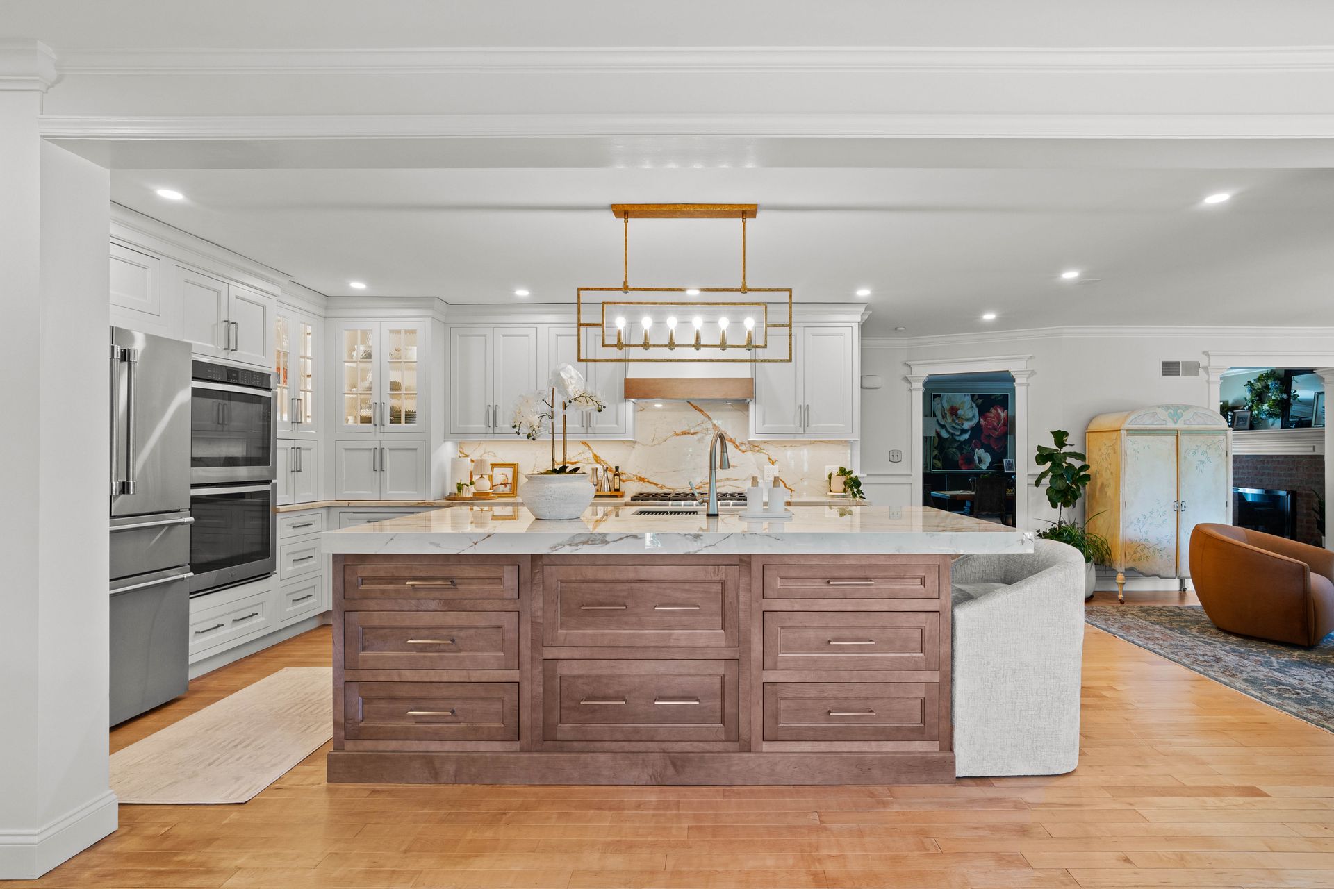 Bright modern kitchen with large island, white cabinetry, marble counters, and warm wood flooring