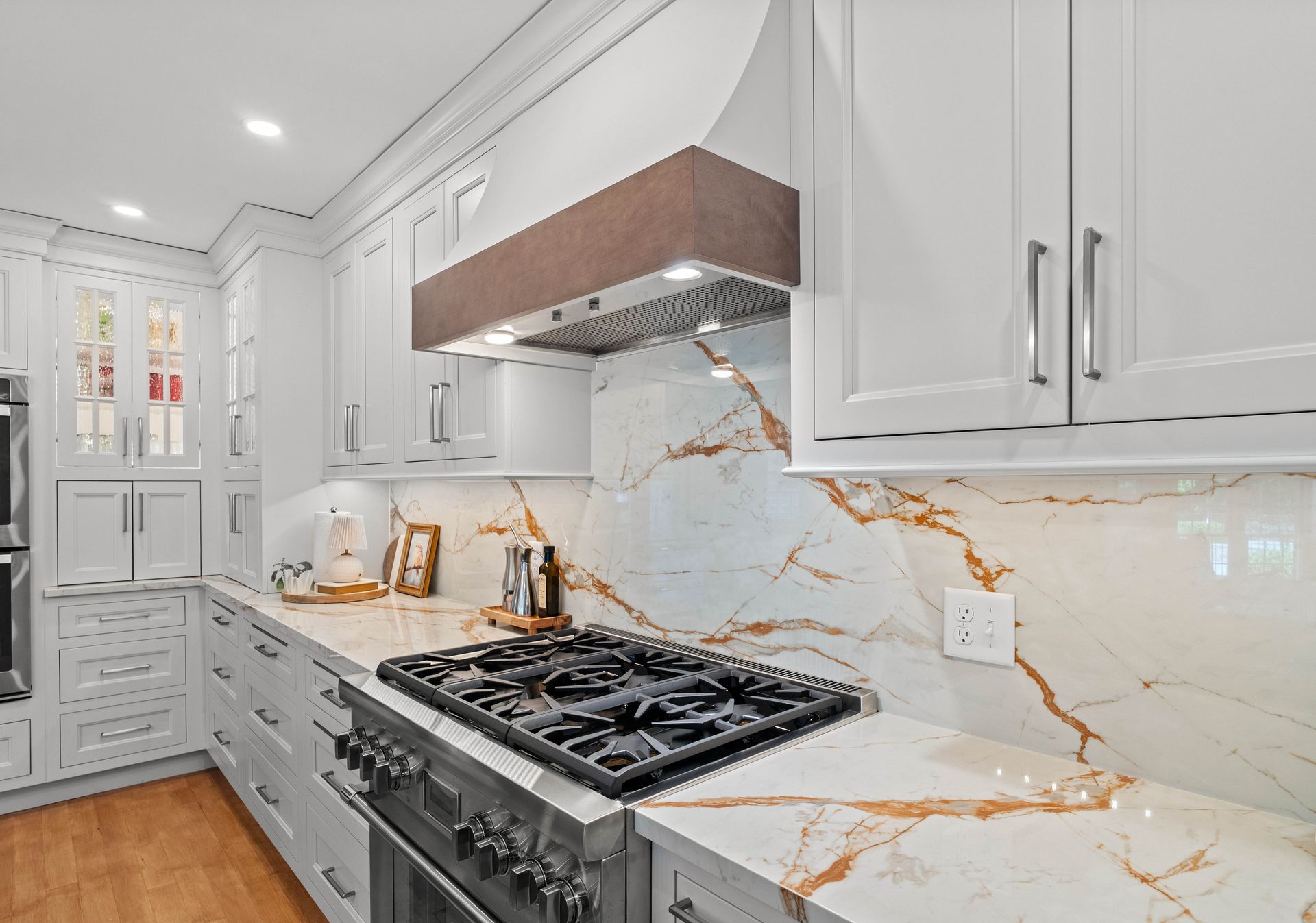 Bright modern white kitchen with marble countertops, gold accents, and a stainless steel gas range