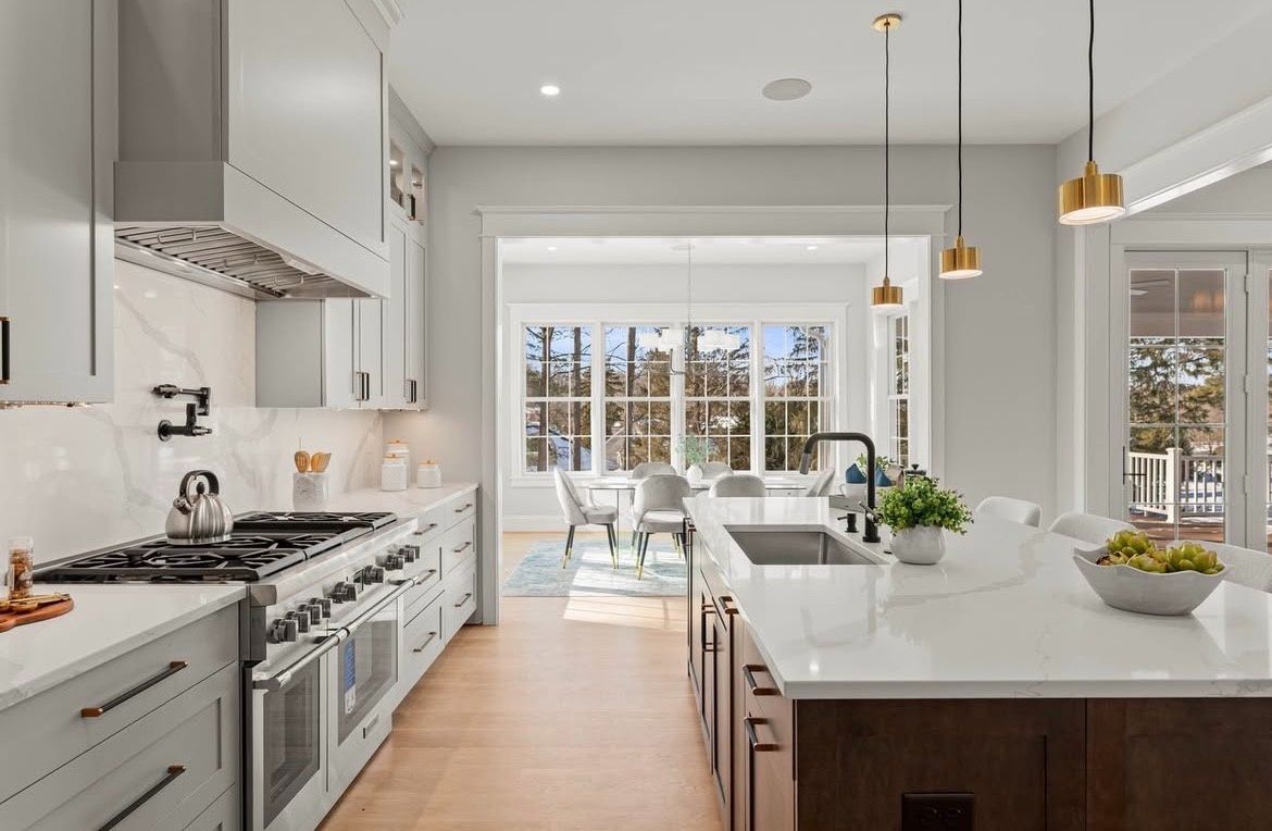 Modern kitchen with gray cabinets, white countertops, and dark wood island, overlooking dining room.