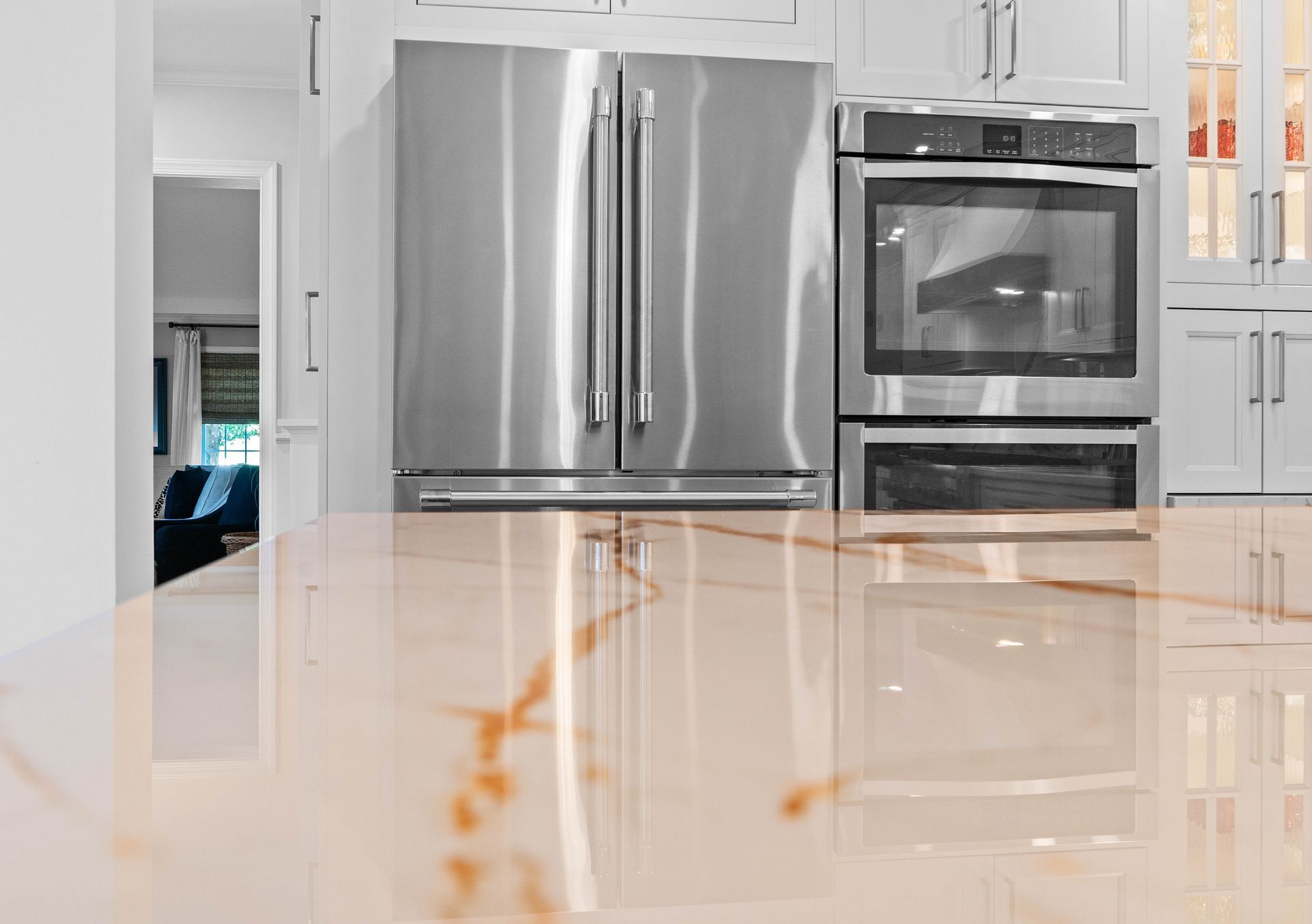 Modern kitchen with stainless steel fridge, oven, and glossy white marble island countertop.