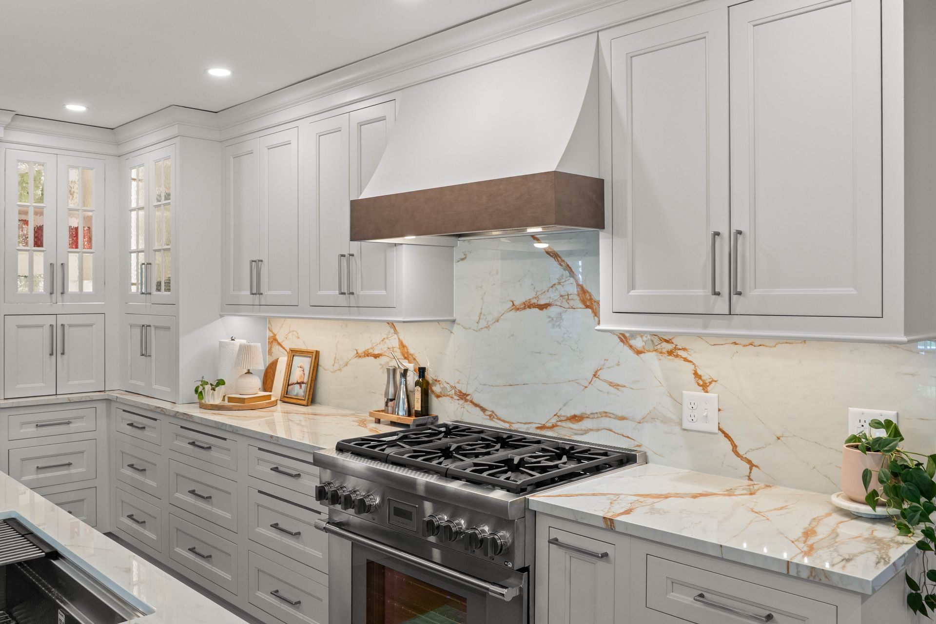 Bright white kitchen with marble backsplash, gray cabinets, and stainless steel stove under a hood